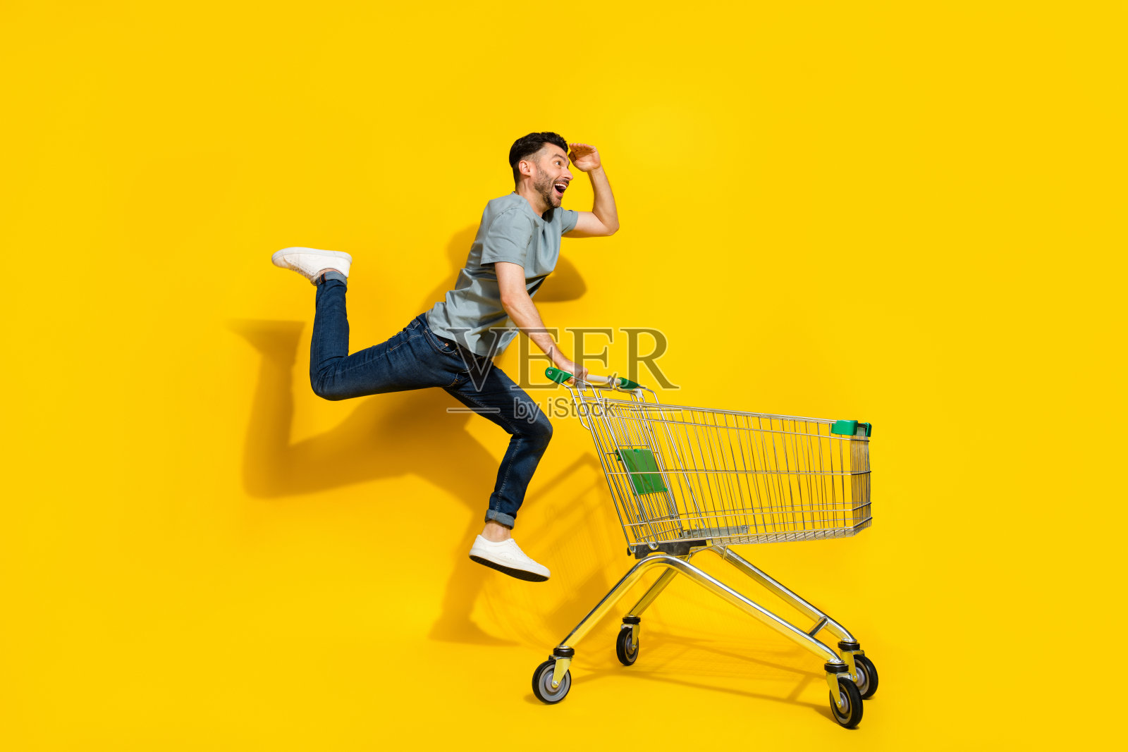 兴奋无忧的人在黄色背景下跳跃，手中拿着空购物车的全身侧面照片照片摄影图片