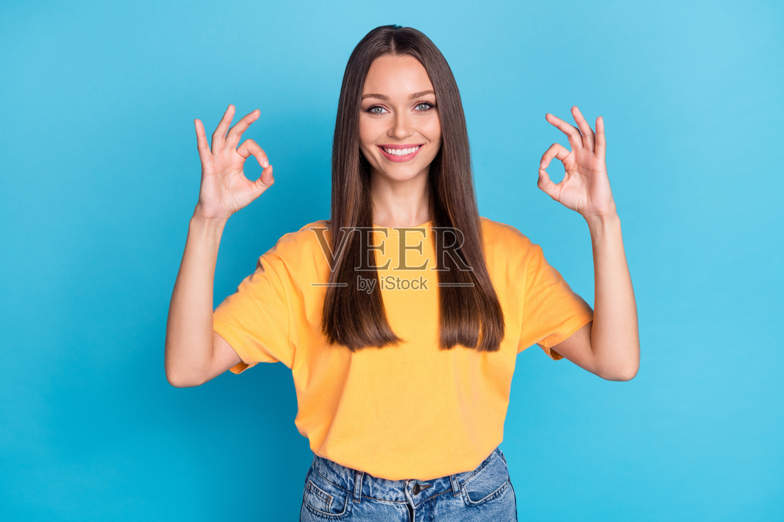 可爱的时尚女士举起双手，做出“好”手势，站在空旷的商店背景前，背景为蓝色。照片摄影图片