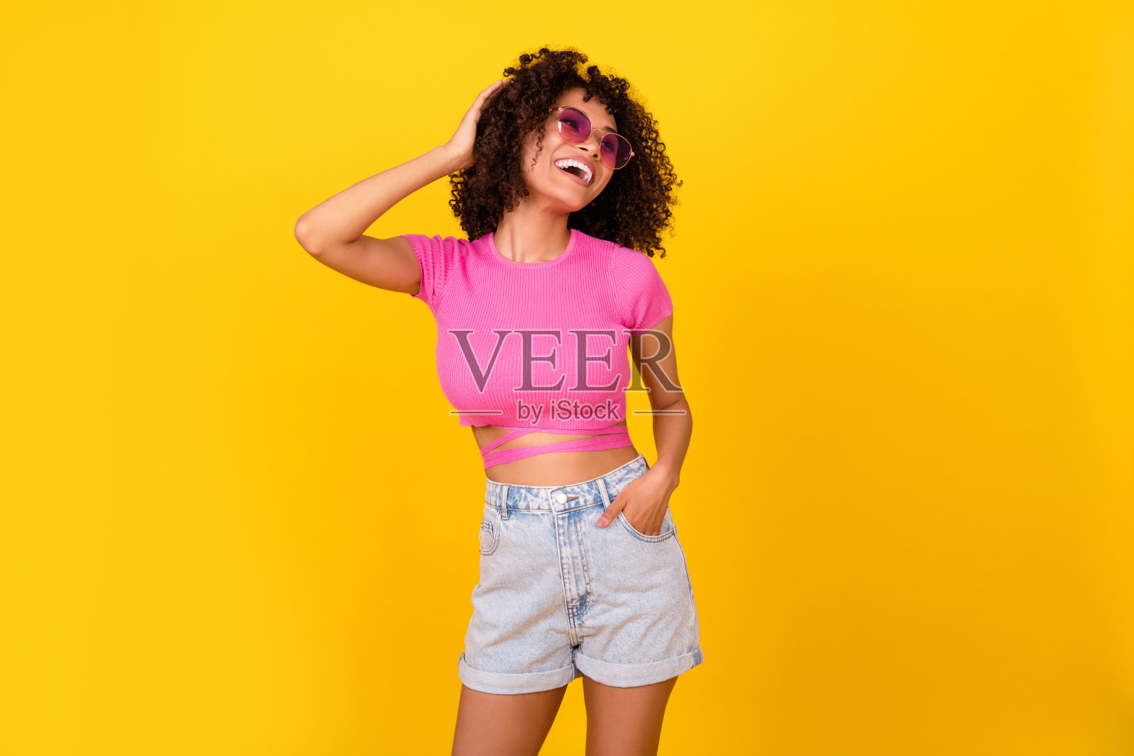 穿着粉色T恤、戴着深色眼镜的可爱搞笑女孩，望着空旷的空间，背景为黄色。照片摄影图片