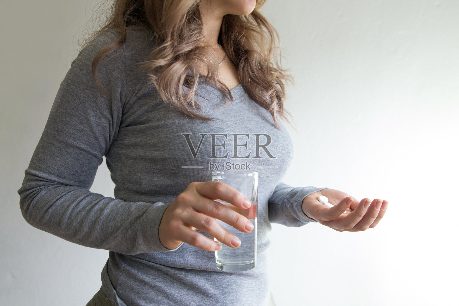 年轻女性在家中用水杯服用药物的特写镜头。照片摄影图片