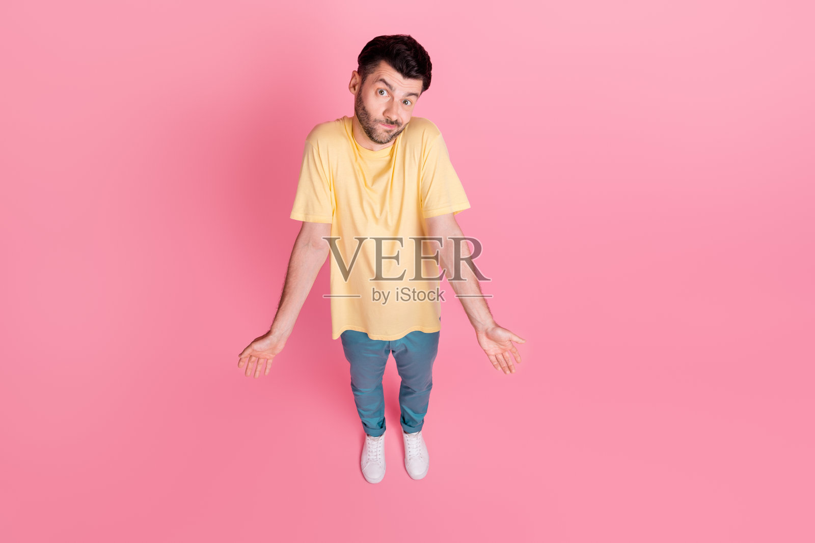 高角度全身照，忧虑紧张的男人耸肩无奈，双手无答，背景为粉色。照片摄影图片