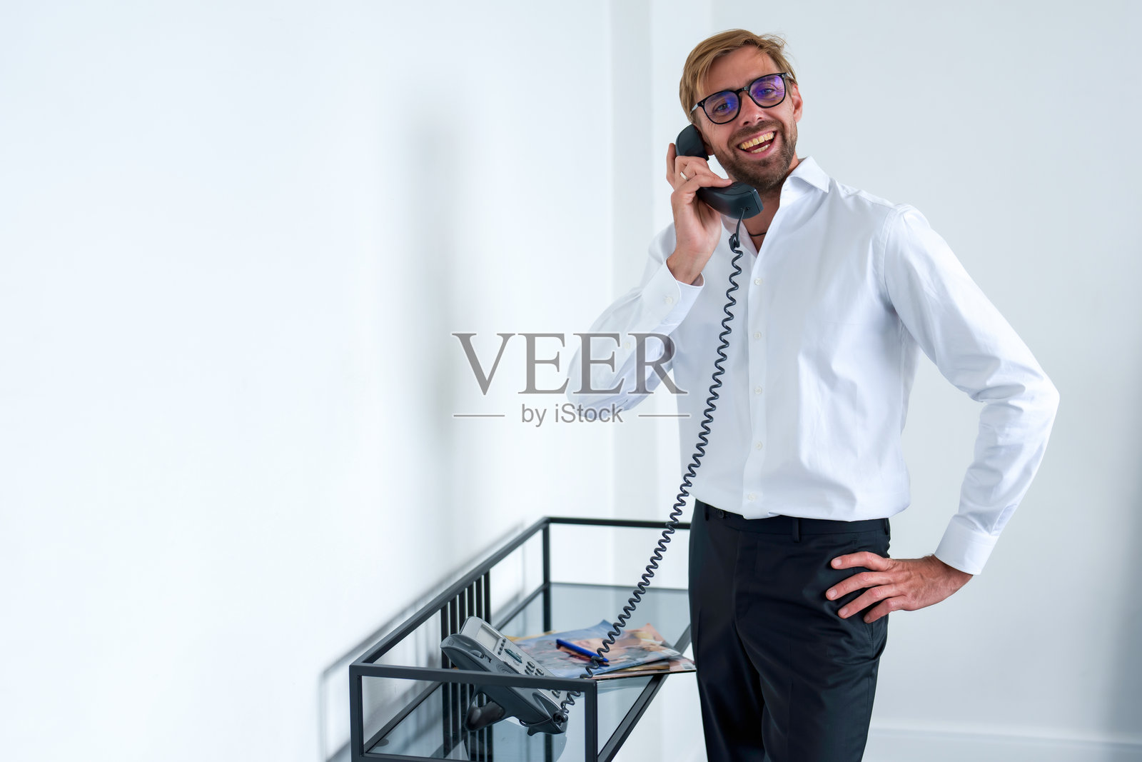 一名男子在白色背景的办公室里通过手机通话。身穿白衬衫的商人正在与手机通话。照片摄影图片