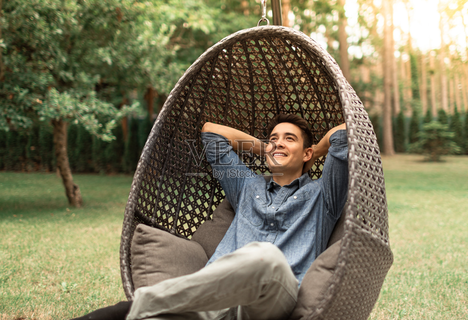 年轻男子坐在舒适的椅子上放松，享受周末的宁静时光，沉浸在大自然中。照片摄影图片