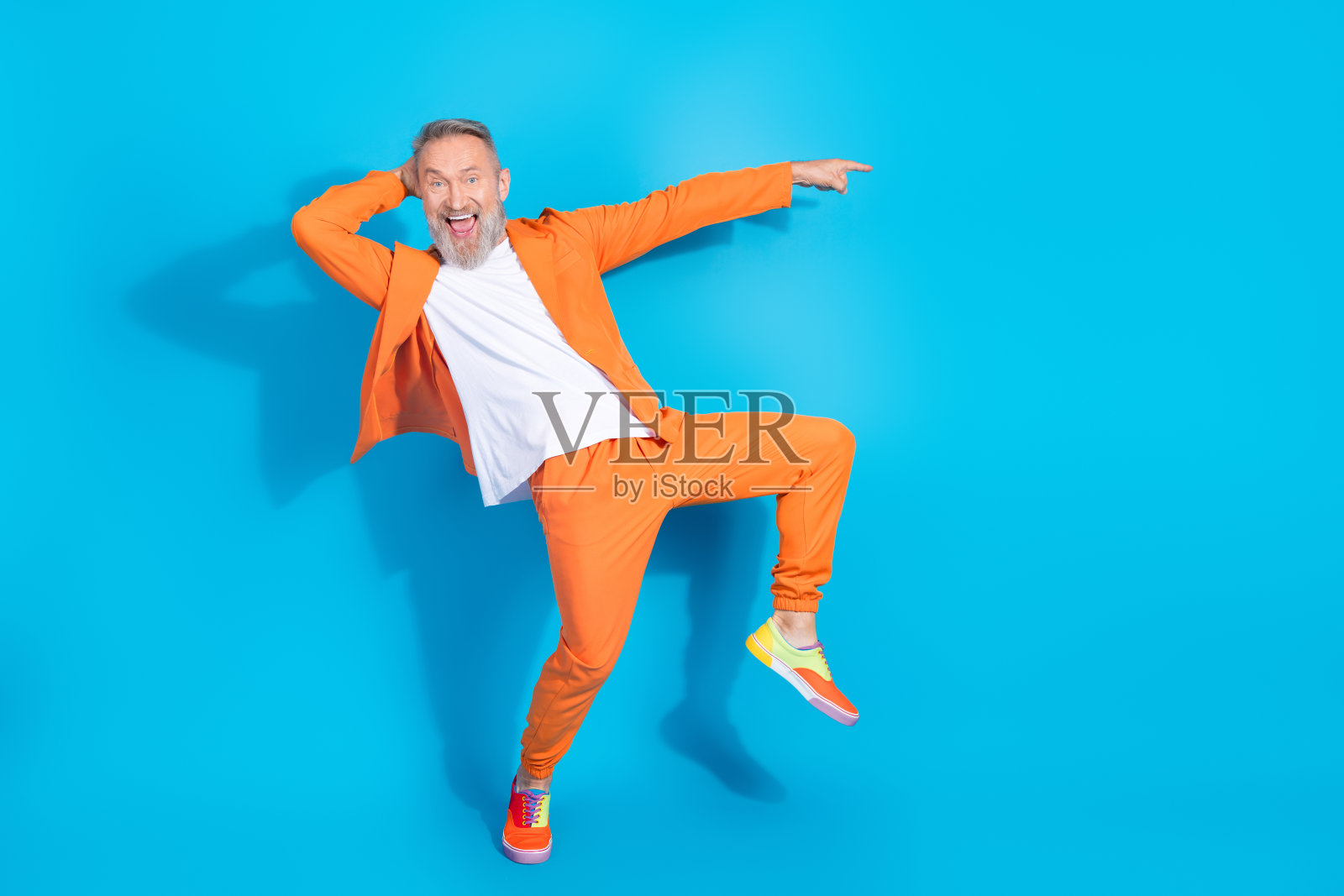全身肖像，穿着橙色西装的时尚老年男士，手指指向空白处，背景为蓝色。照片摄影图片