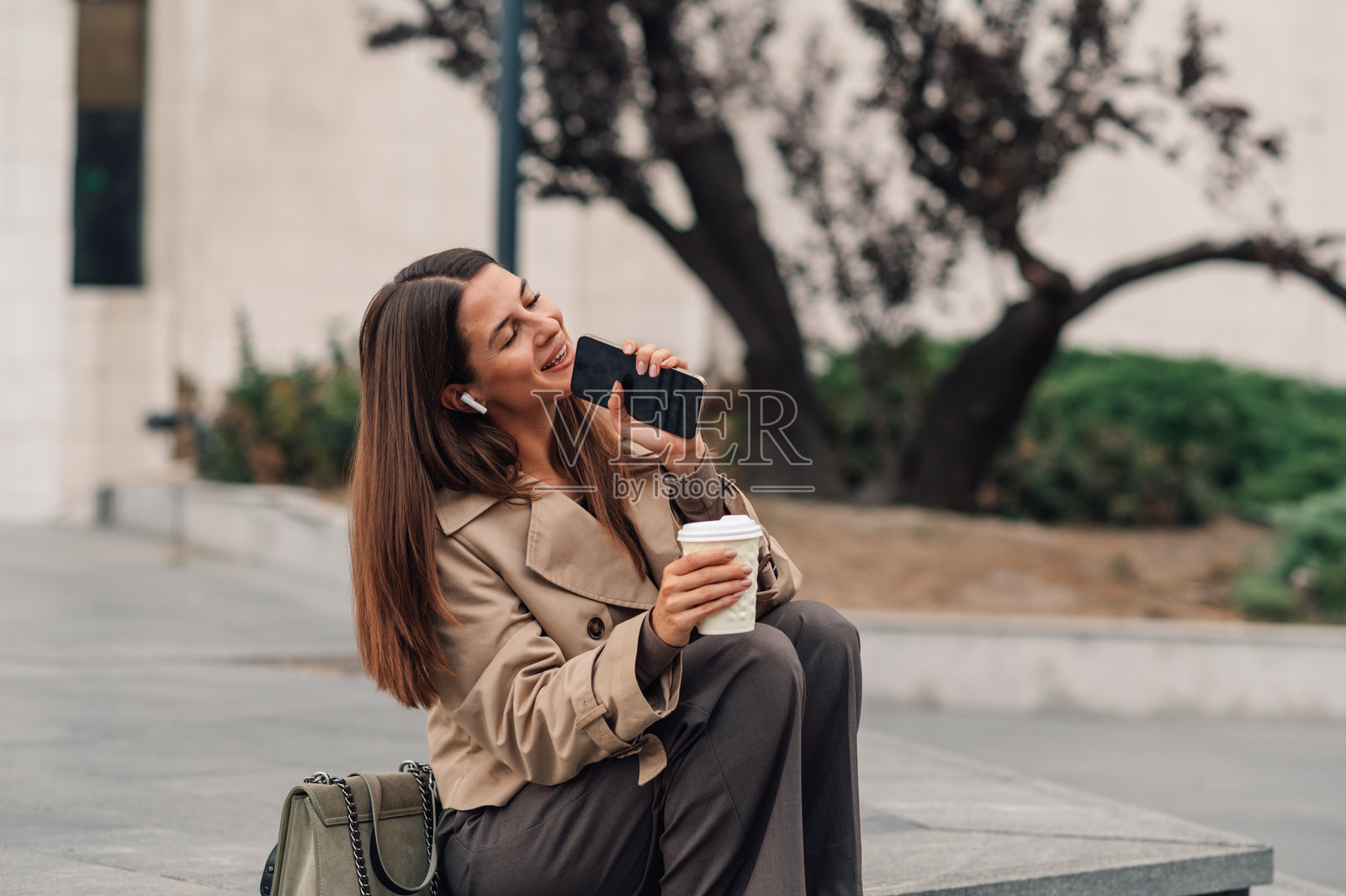 商务女性在户外用智能手机听音乐并喝咖啡照片摄影图片