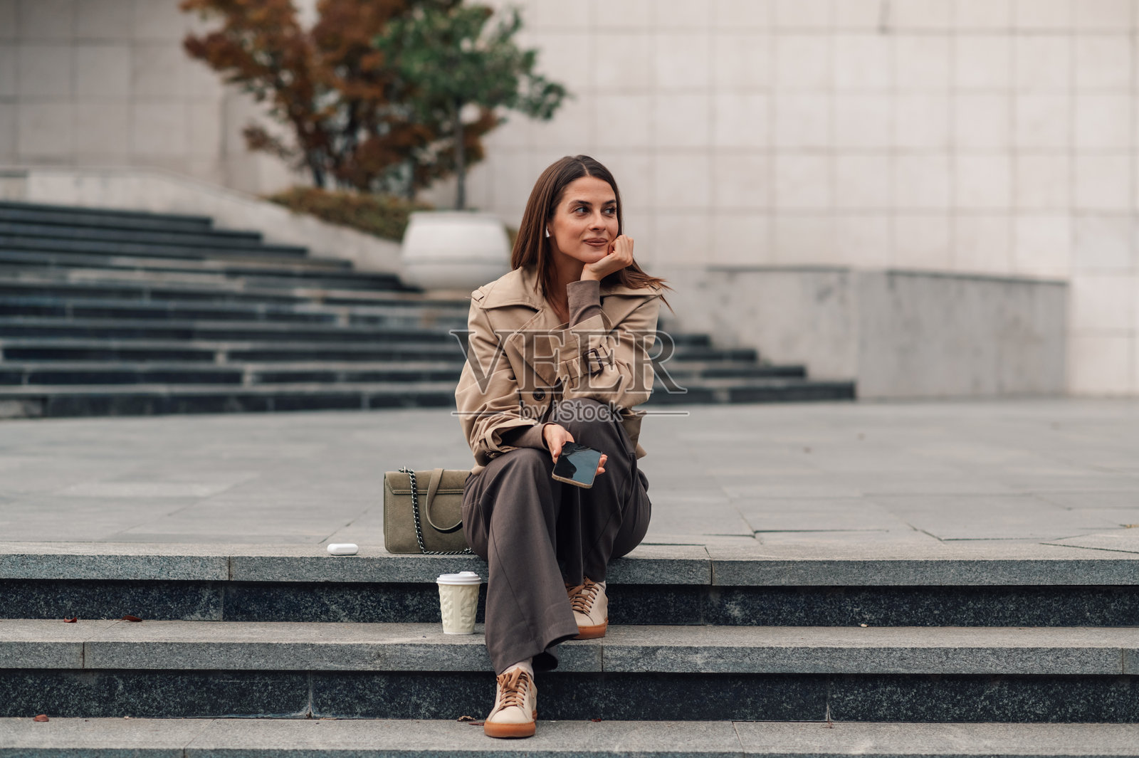 女商人在楼梯上休息，手里拿着智能手机。照片摄影图片