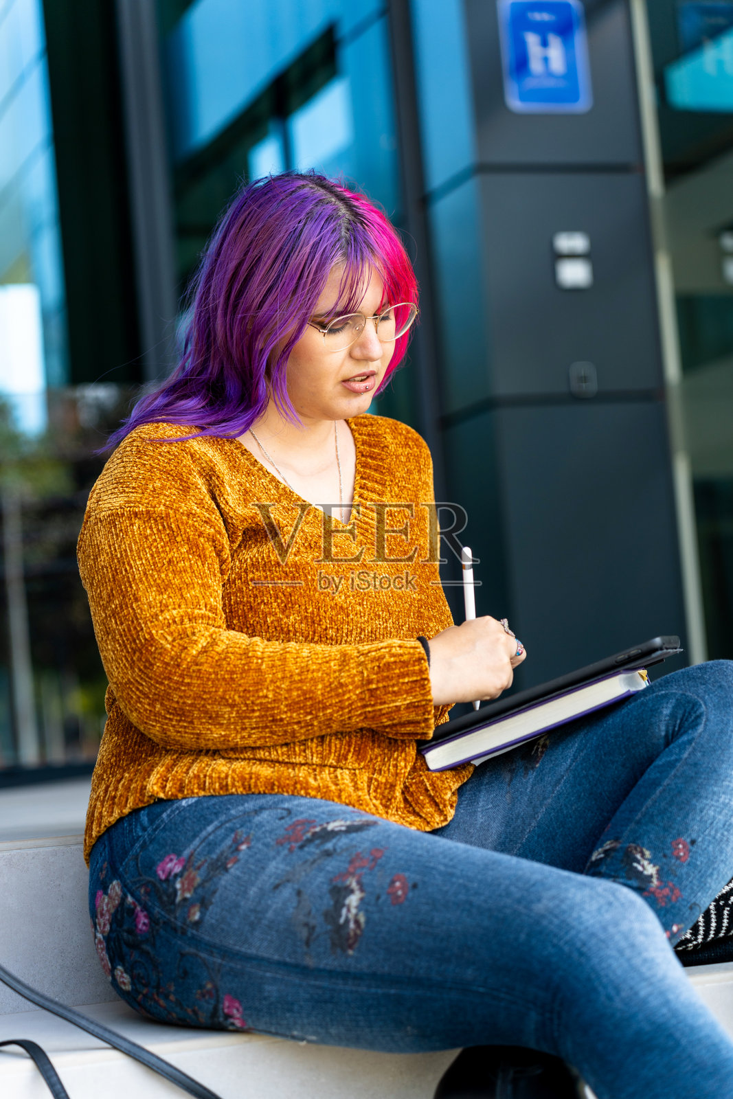 一位拥有粉色头发的自信自闭症女孩坐在酒店门口，用平板电脑绘画。照片摄影图片