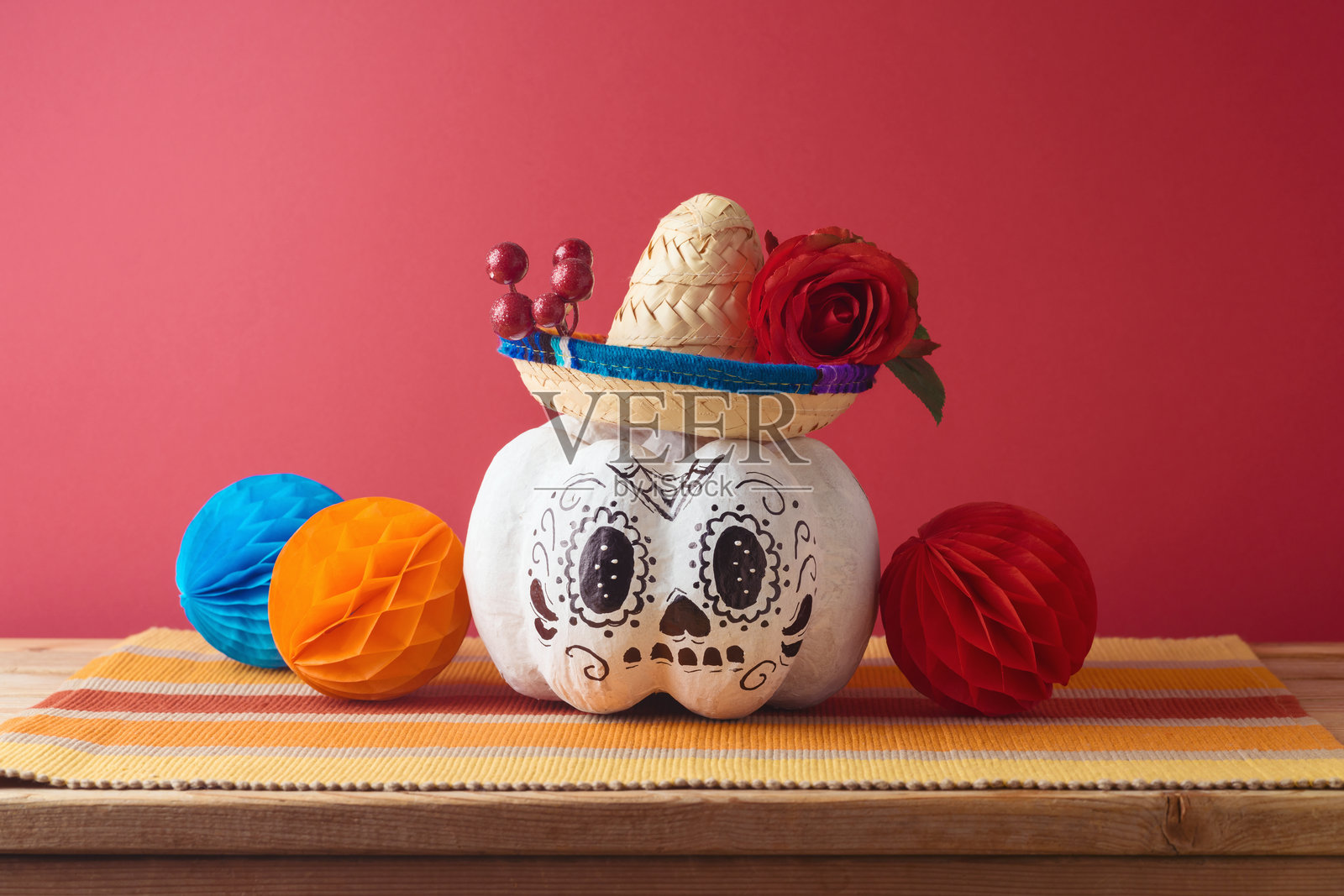 亡灵节，亡灵节假日概念。糖骷髅、万圣节南瓜和墨西哥派对帽子放在粉色背景的木桌上。照片摄影图片