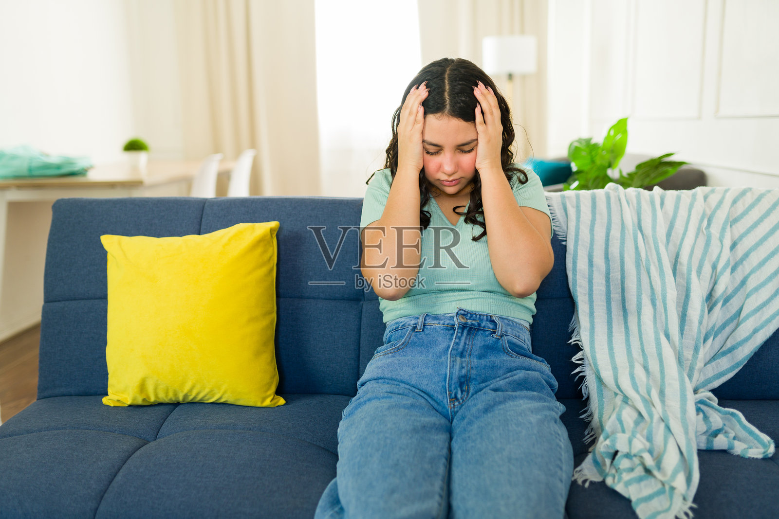 一名女性青少年在家中的舒适沙发上坐着，感到偏头痛并捂着头。照片摄影图片