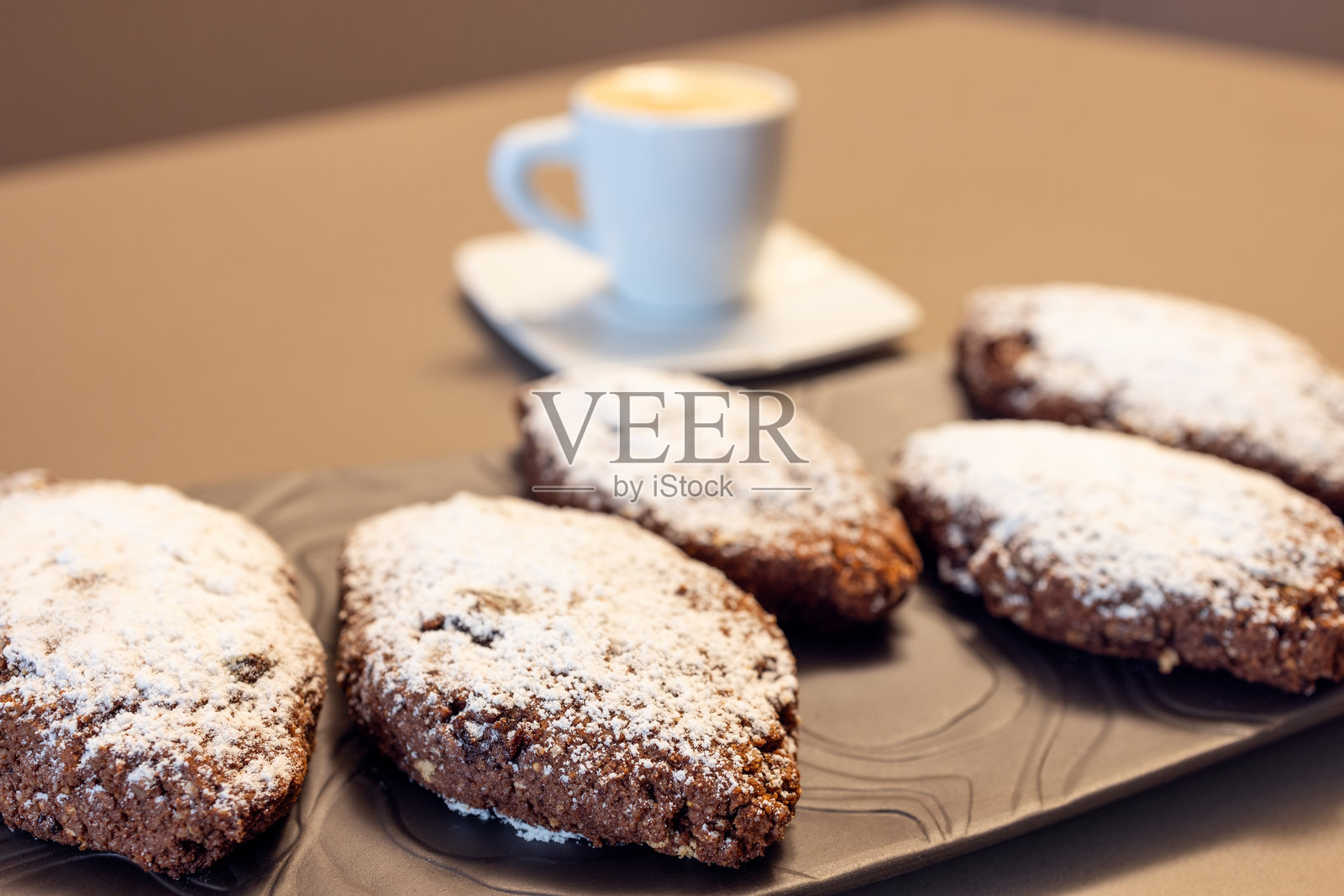 意大利的死亡面包饼干，上面撒有糖粉，摆放在深色盘子上，背景中有一杯模糊的浓缩咖啡。照片摄影图片