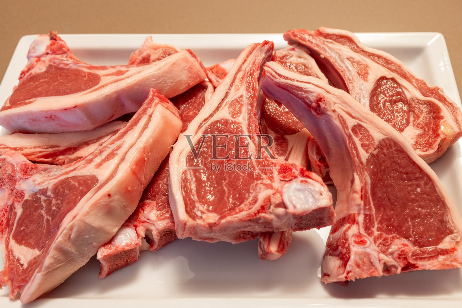 高质量的新西兰羊肋排整齐地摆放在白色盘子上，肉质鲜嫩的粉红色和脂肪层突显了肋排的新鲜和极佳的嫩度，适合烧烤。照片摄影图片