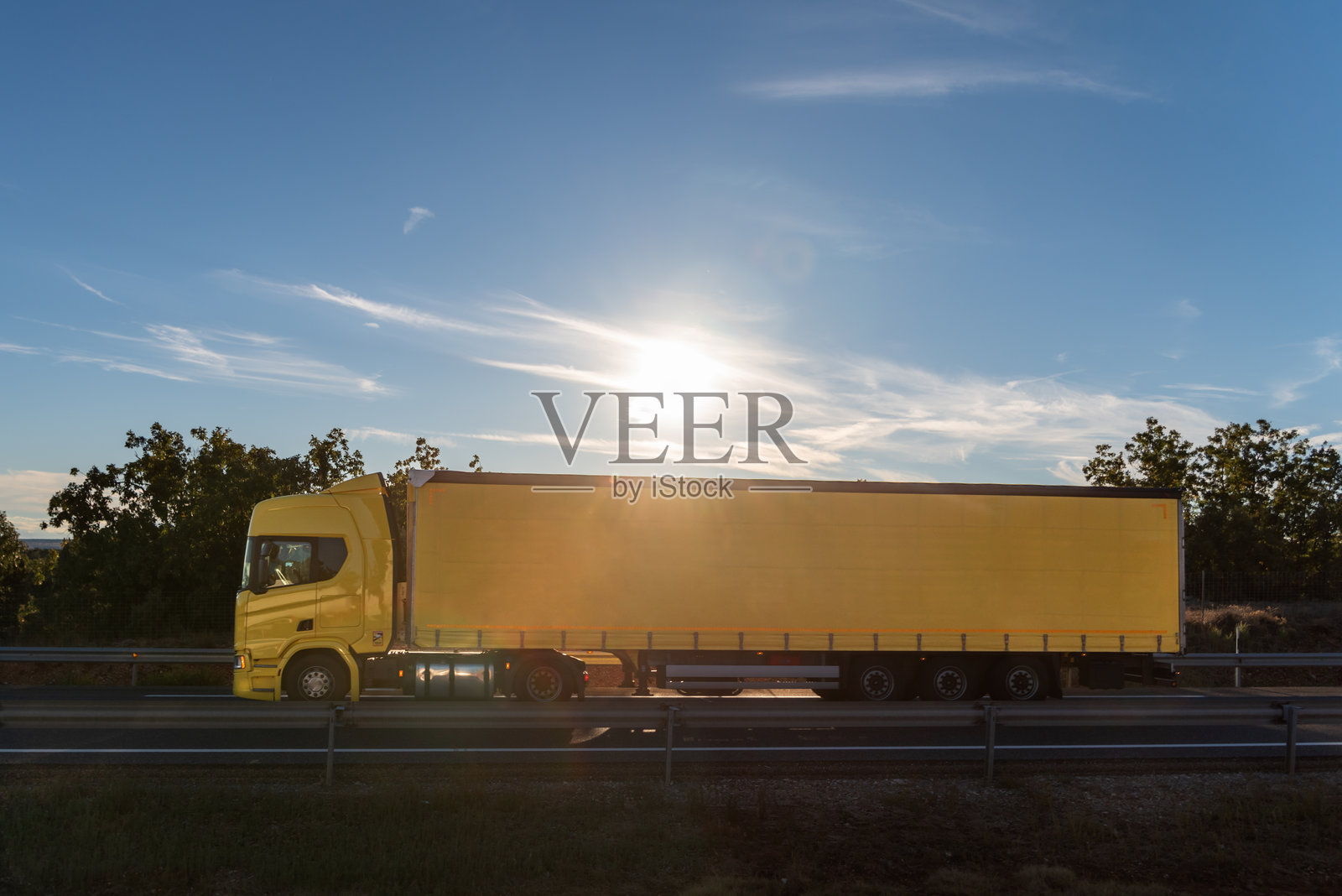 蓝天下，阳光照耀下的黄色篷布卡车侧面视图。照片摄影图片