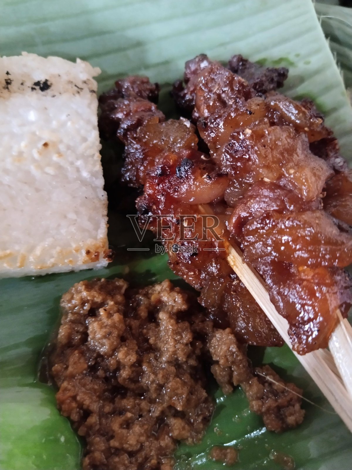 特写的羊肉沙爹（Sate Kambing），配有番茄、青葱、青辣椒和甜酱油，摆放在圆形白盘上。印尼传统美食。照片摄影图片