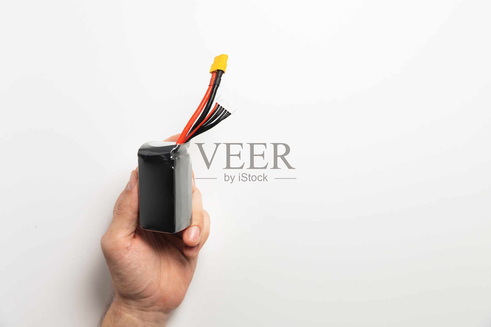 一个男人手中拿着带有平衡和电源连接器的锂聚合物电池，用于为FPV无人机供电照片摄影图片
