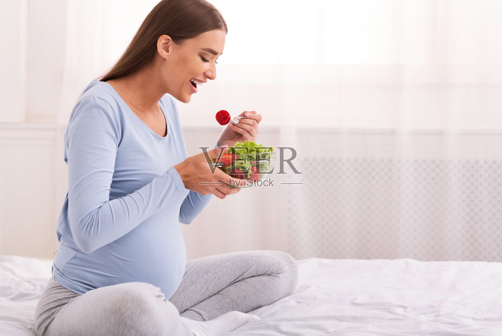 饥饿的孕妇在床上享用蔬菜沙拉照片摄影图片