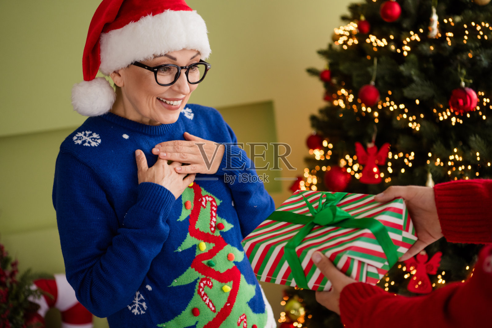 可爱的老年女性穿着蓝色毛衣，在温馨的室内气氛中收到圣诞礼物，感受新年的魔力和圣诞精神。照片摄影图片