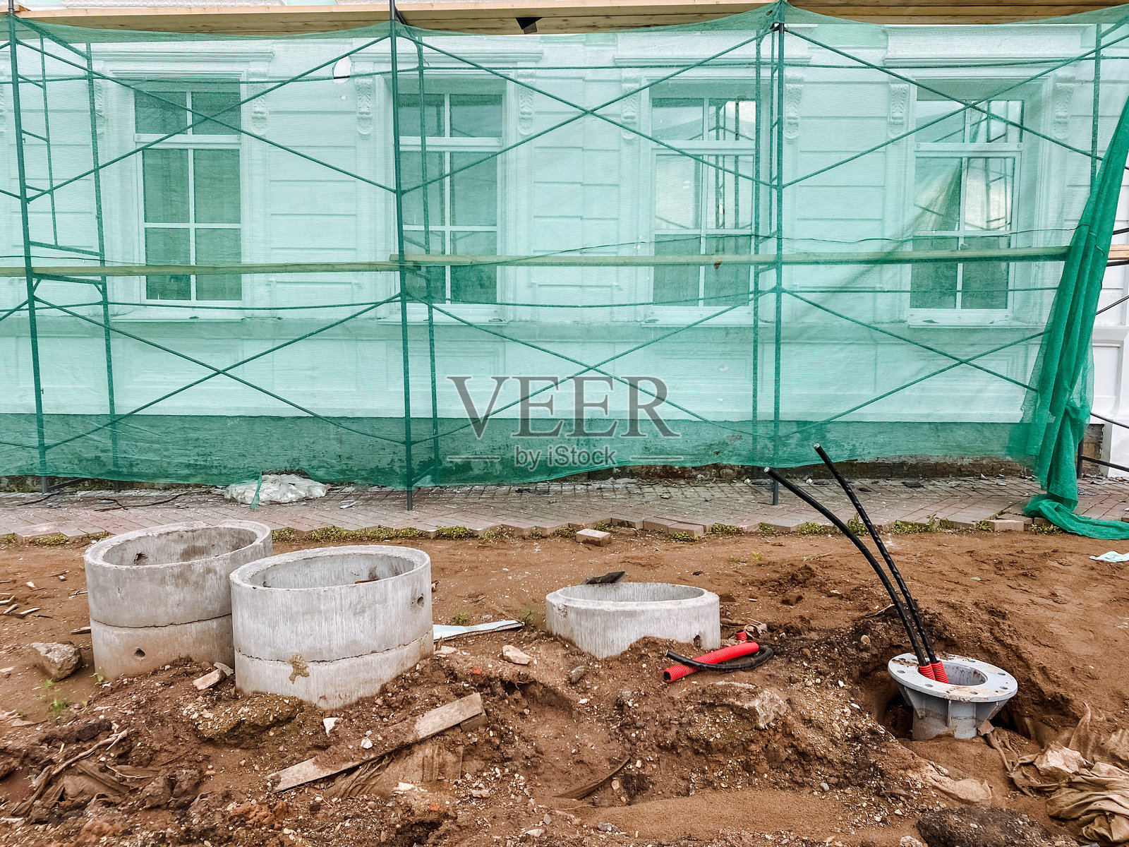 一个建筑工地，设有脚手架和埋在土中的混凝土环，周围有各种与建筑和园艺活动相关的材料和元素。照片摄影图片