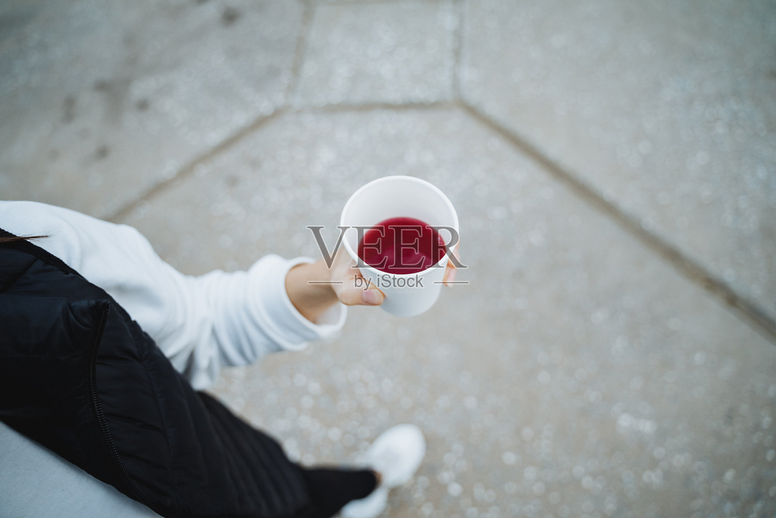 一个人自信地举着一杯充满鲜艳夺目的红色液体，吸引了附近人们的好奇和注意，他们注意到了这个引人注目的饮品选择。照片摄影图片