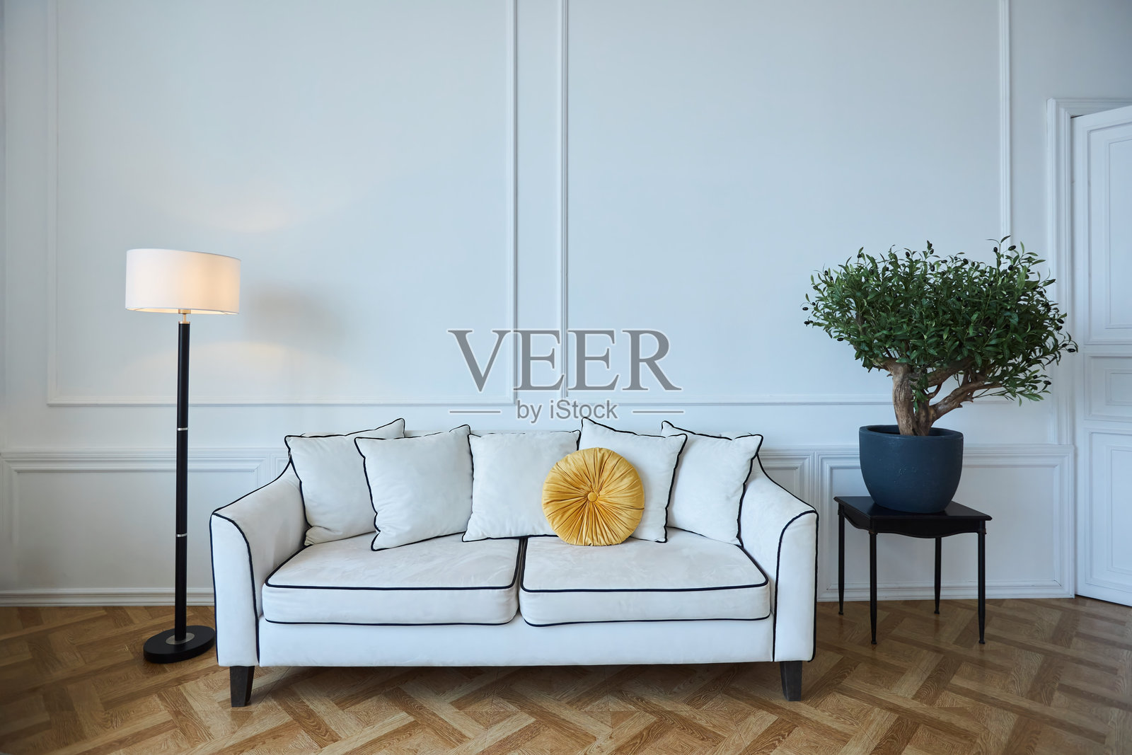 一张白色沙发上放着一个黄色的枕头，坐落在一扇大窗户前。沙发旁的地板上有一盆植物。房间光线充足，给人一种干净、简约的感觉。照片摄影图片