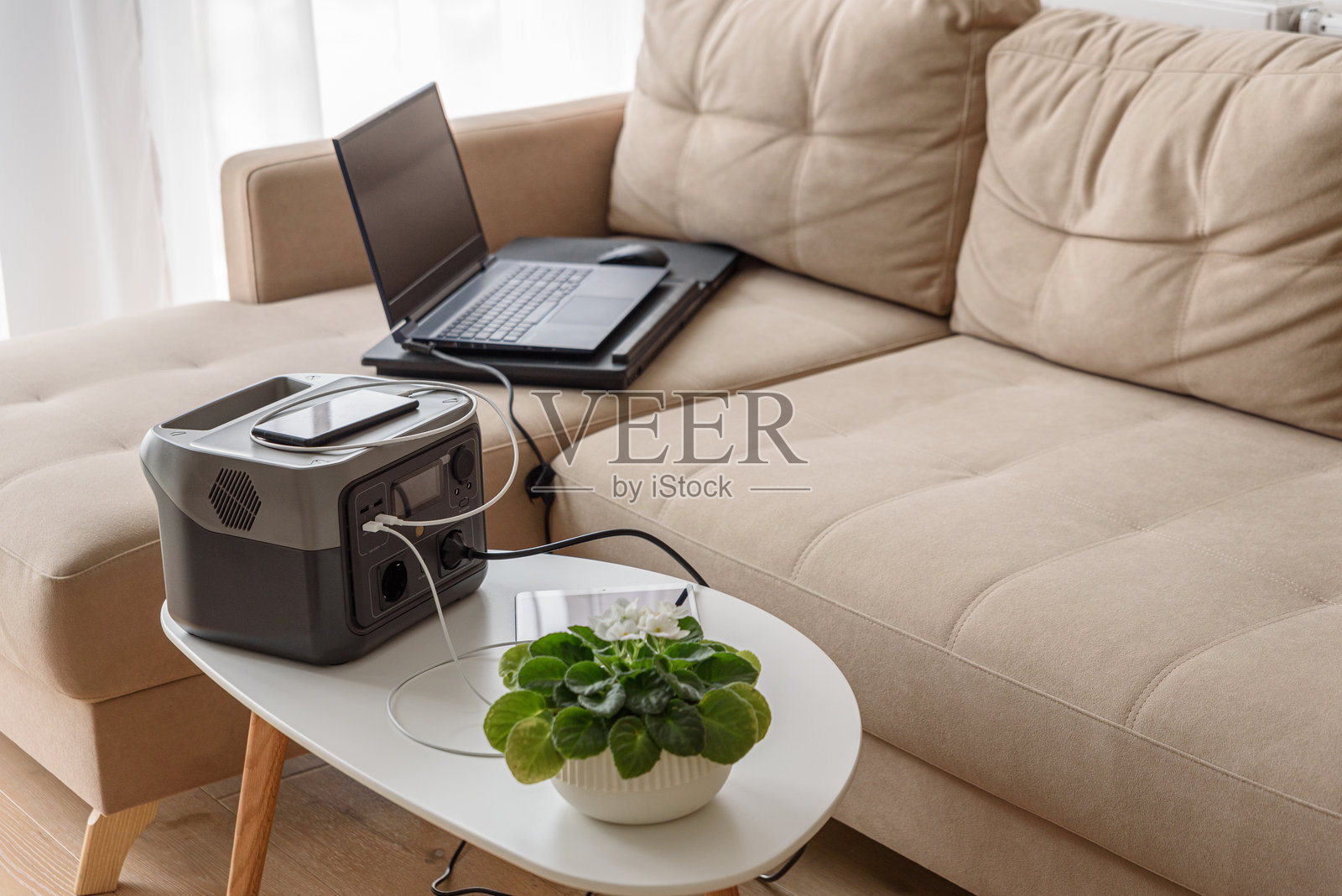 不间断电源。沙发上的工作空间，配有笔记本电脑、平板电脑、智能手机和便携式电源站。照片摄影图片