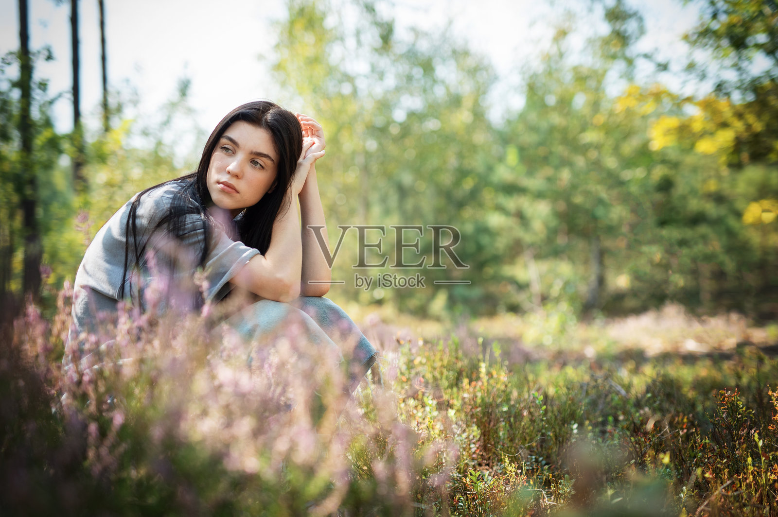 一位年轻女性在阳光明媚的日子里，静静地坐在宁静的森林空地上，四周环绕着五彩斑斓的野花。照片摄影图片