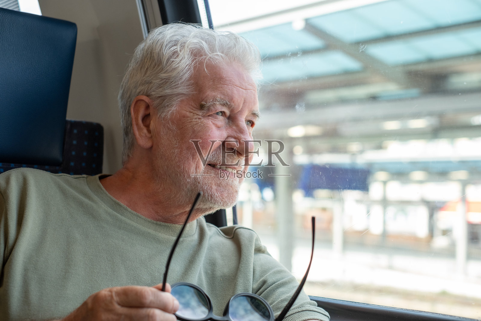 微笑的胡子老年男子坐在火车上，享受旅途中的时光，望着窗外，悠闲地欣赏着经过的风景。照片摄影图片