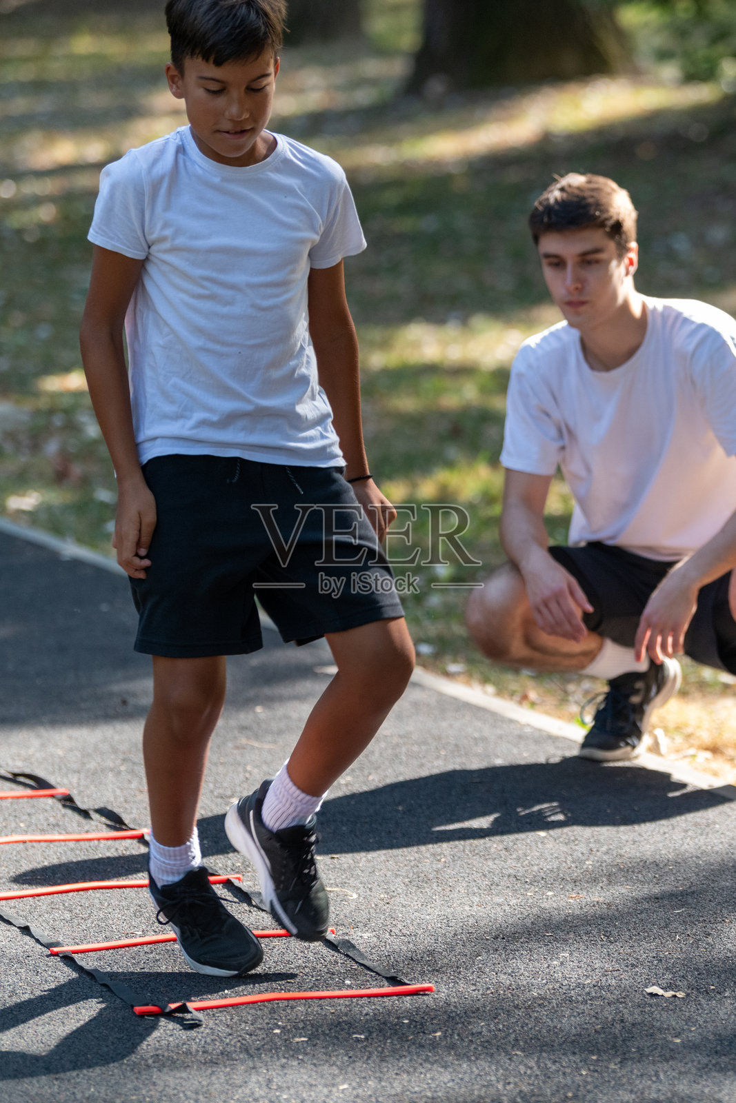男孩在户外与教练一起练习敏捷梯训练，专注于提高速度、协调性和体能。开放的环境强调了儿童积极、健康和有趣的身体锻炼。照片摄影图片