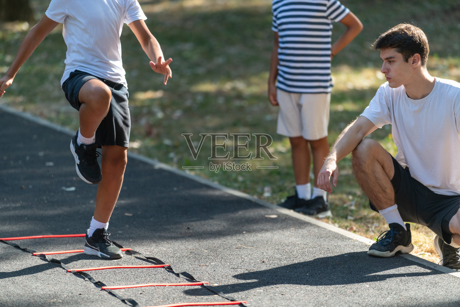 男孩在户外与教练一起练习敏捷梯训练，专注于提高速度、协调性和体能。开放的环境强调了儿童积极、健康和有趣的身体锻炼。照片摄影图片