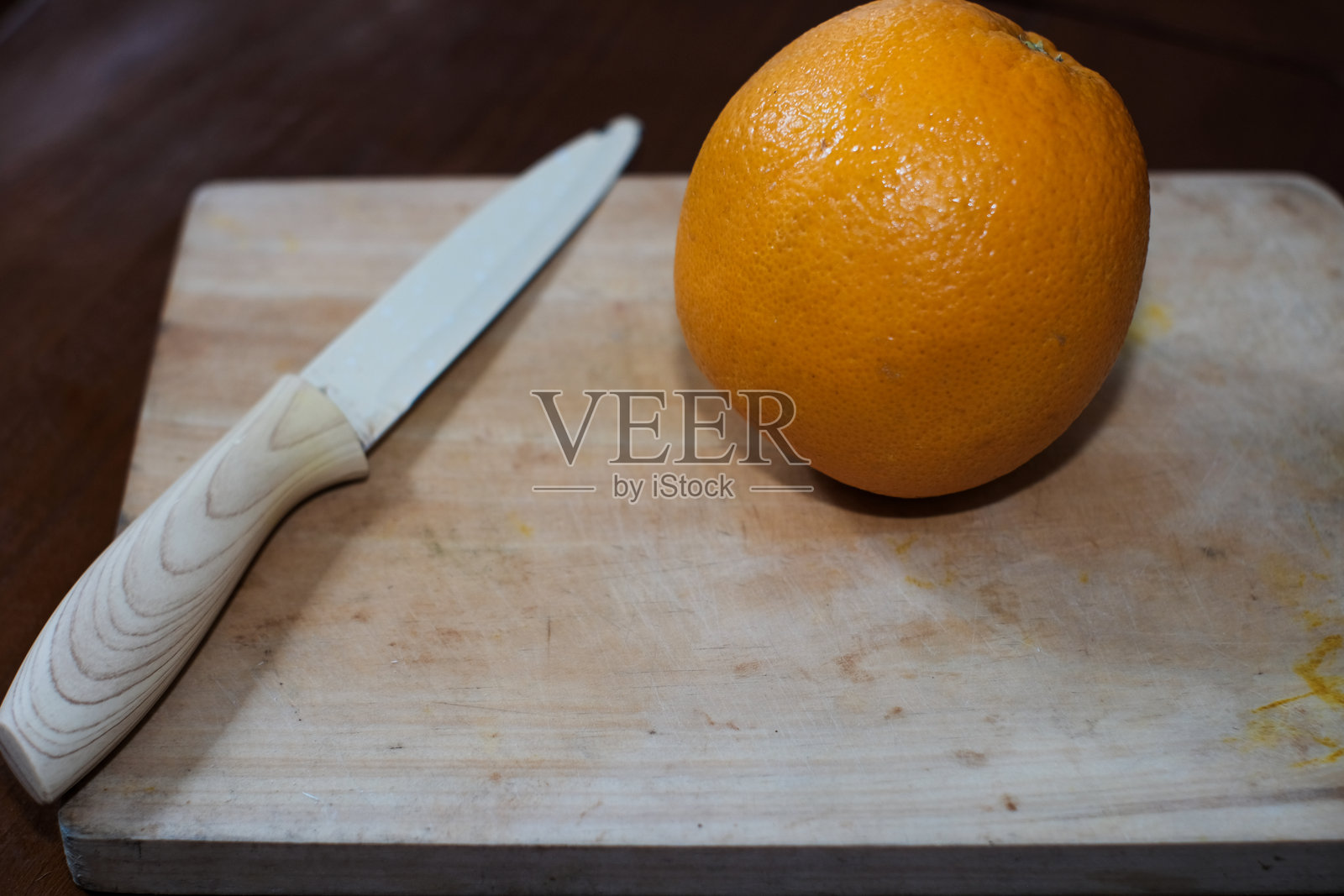 一颗大而多汁的明亮橙子，旁边放着刀，放在木质切菜板上，位于木桌上。照片摄影图片