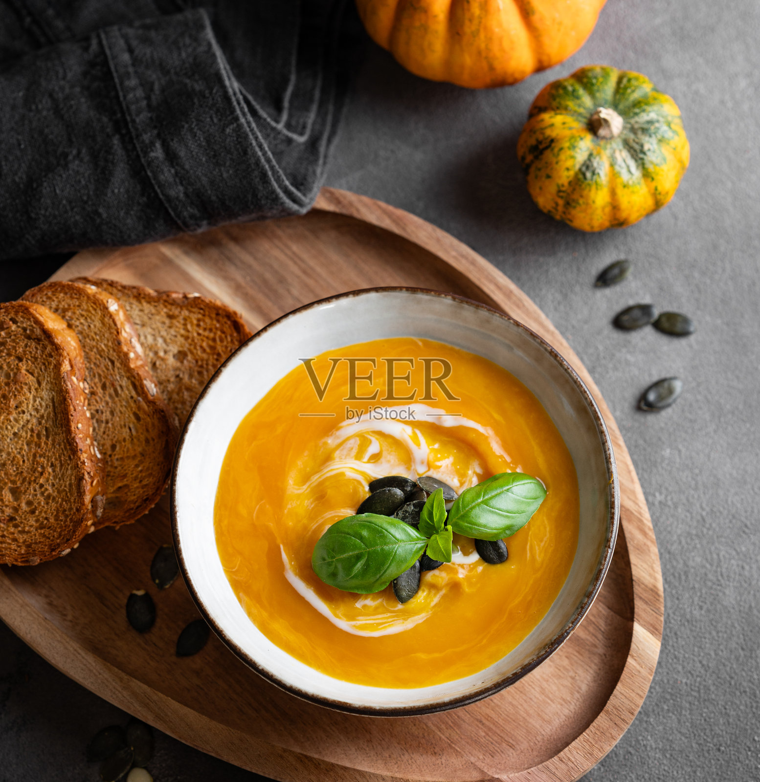 南瓜汤配奶油、罗勒和种子，放在木板上，旁边有炸面包，背景为深色。照片摄影图片