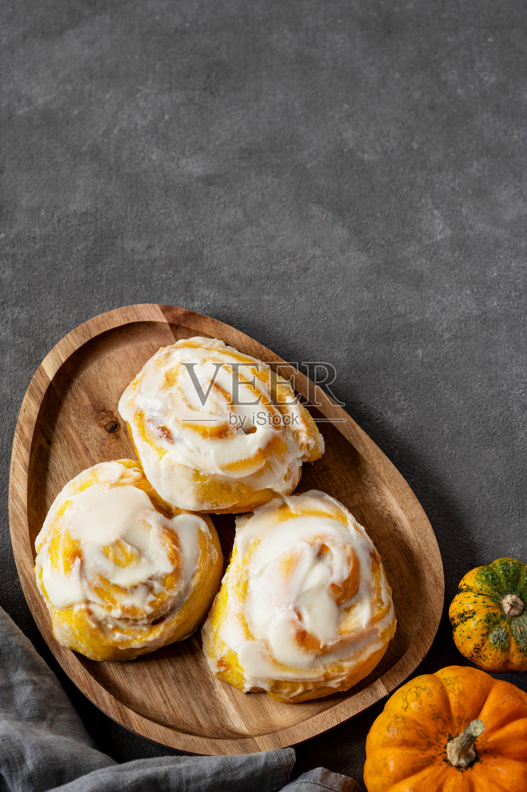 木盘上放着带有奶油糖霜和肉桂的南瓜卷，背景为深色。照片摄影图片