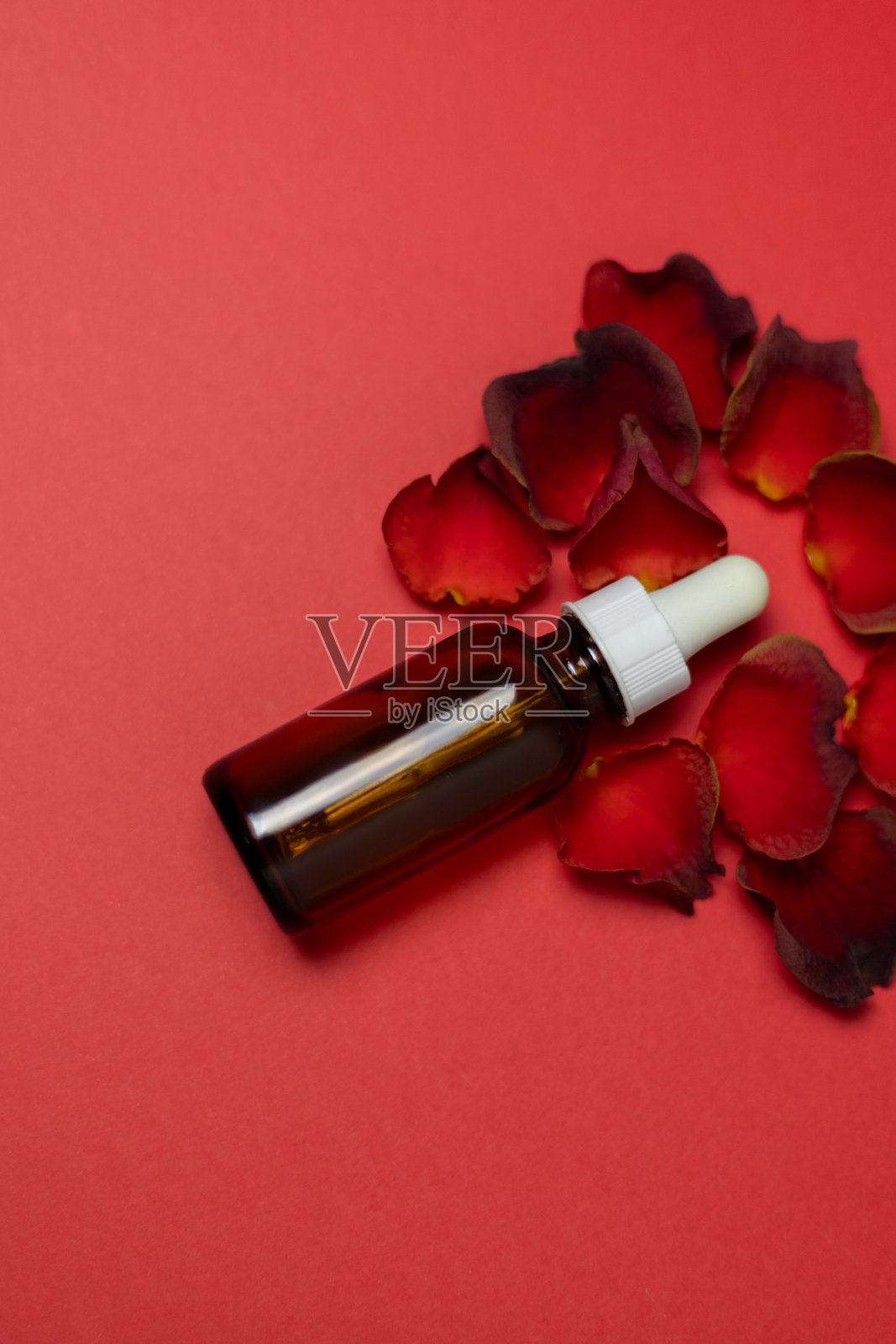 红色背景上的化妆品精华瓶与红玫瑰花瓣照片摄影图片