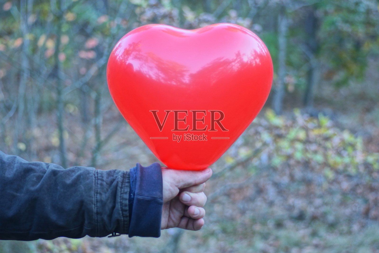 一只穿着黑色衣服的手握着一个红色心形气球照片摄影图片