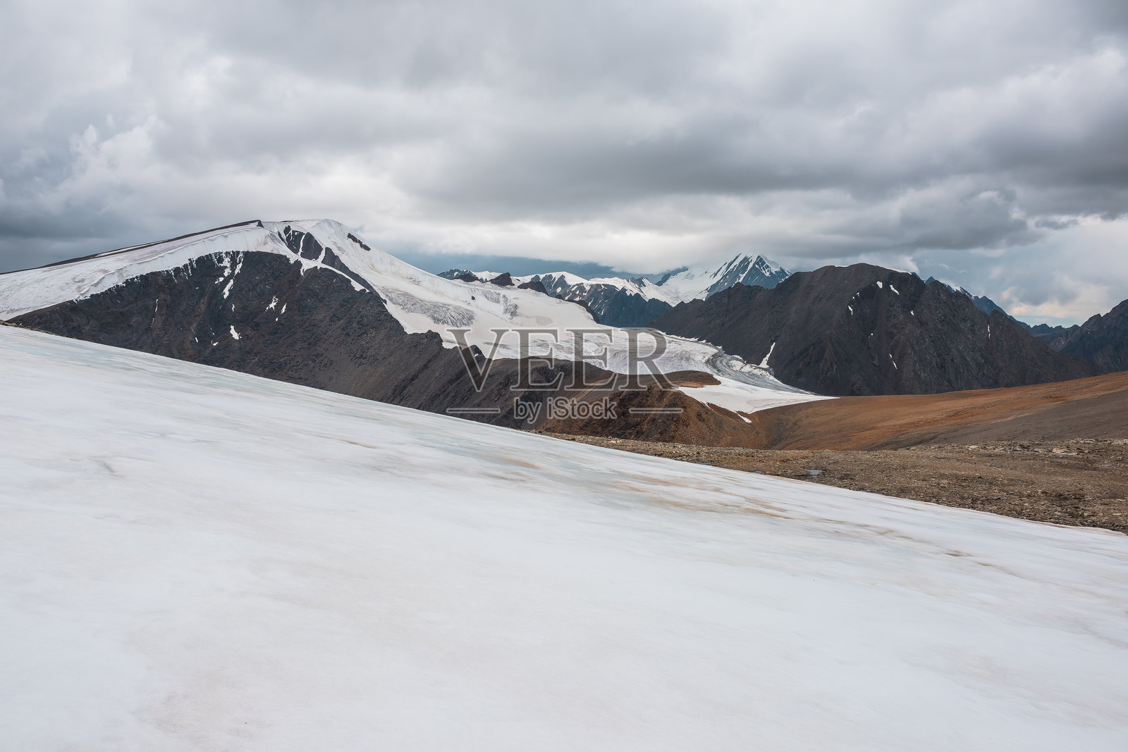戏剧性的阿尔卑斯山景观，巨大的冰川舌头在尖锐的岩石和高耸的雪山顶之间，低沉的雨云笼罩。冰与陡峭的岩壁。高雪山中的氛围景观，灰色多云的天空。照片摄影图片