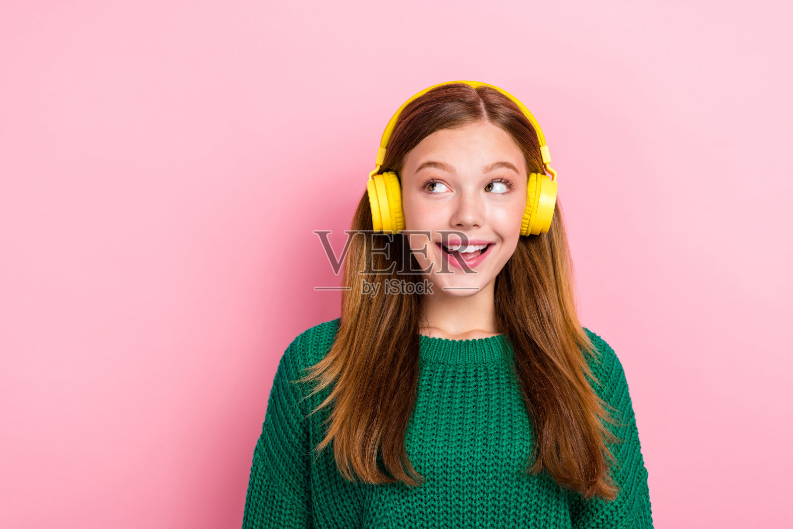 特写照片：年轻、兴奋、积极的女孩，穿着绿色毛衣，梦幻般的神情，空旷的空间，聆听新的音轨，背景为粉色。照片摄影图片