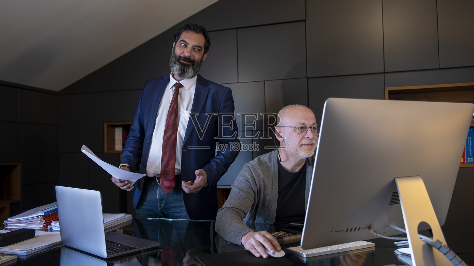 两位中年商人在办公室的桌子上愉快地会面并使用电脑工作。照片摄影图片