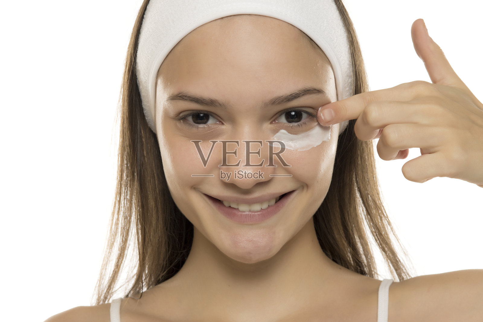 美丽。年轻微笑的女性在白色背景下涂抹眼部化妆霜。照片摄影图片