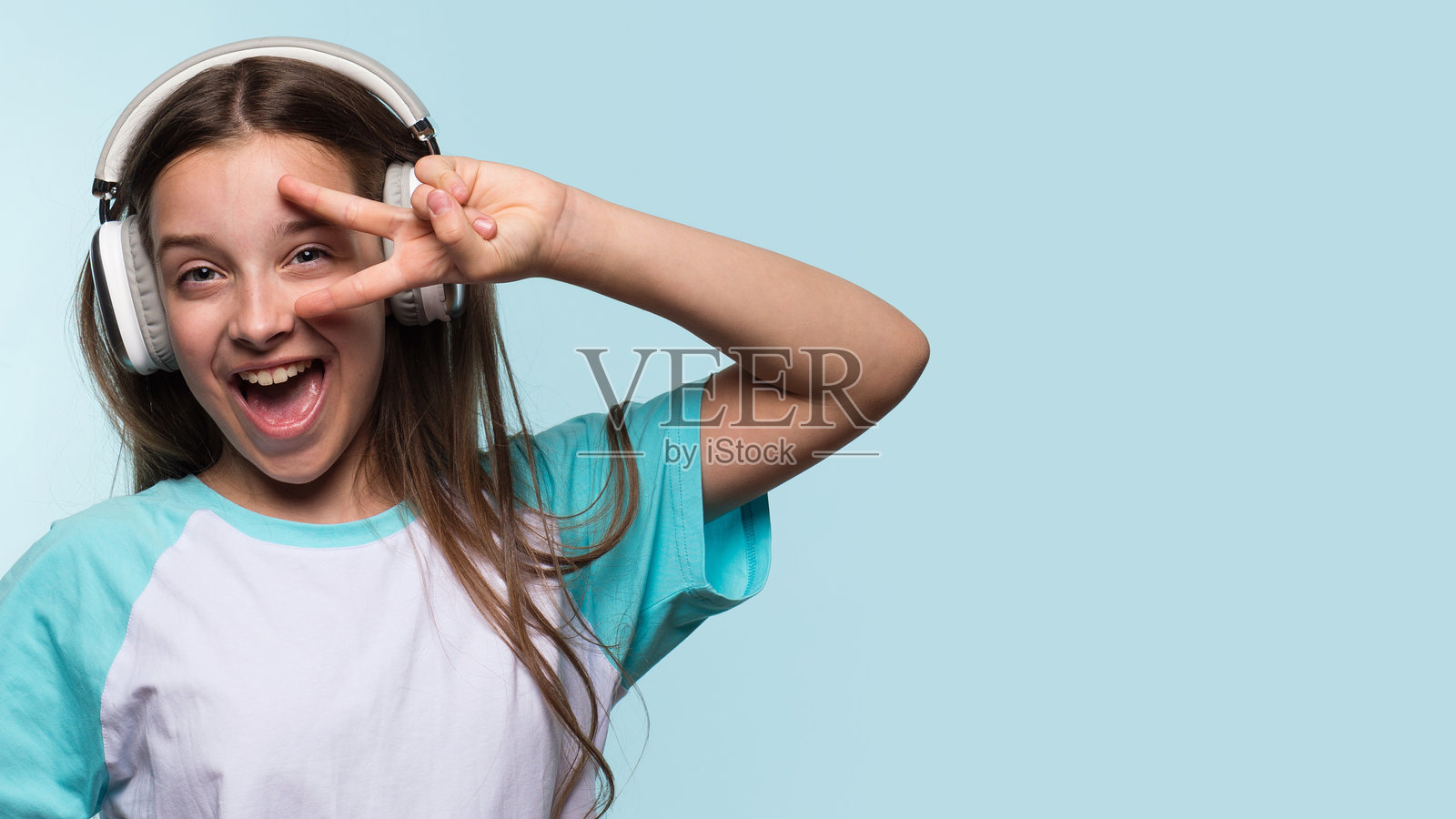 快乐的女孩戴着耳机做出和平手势照片摄影图片