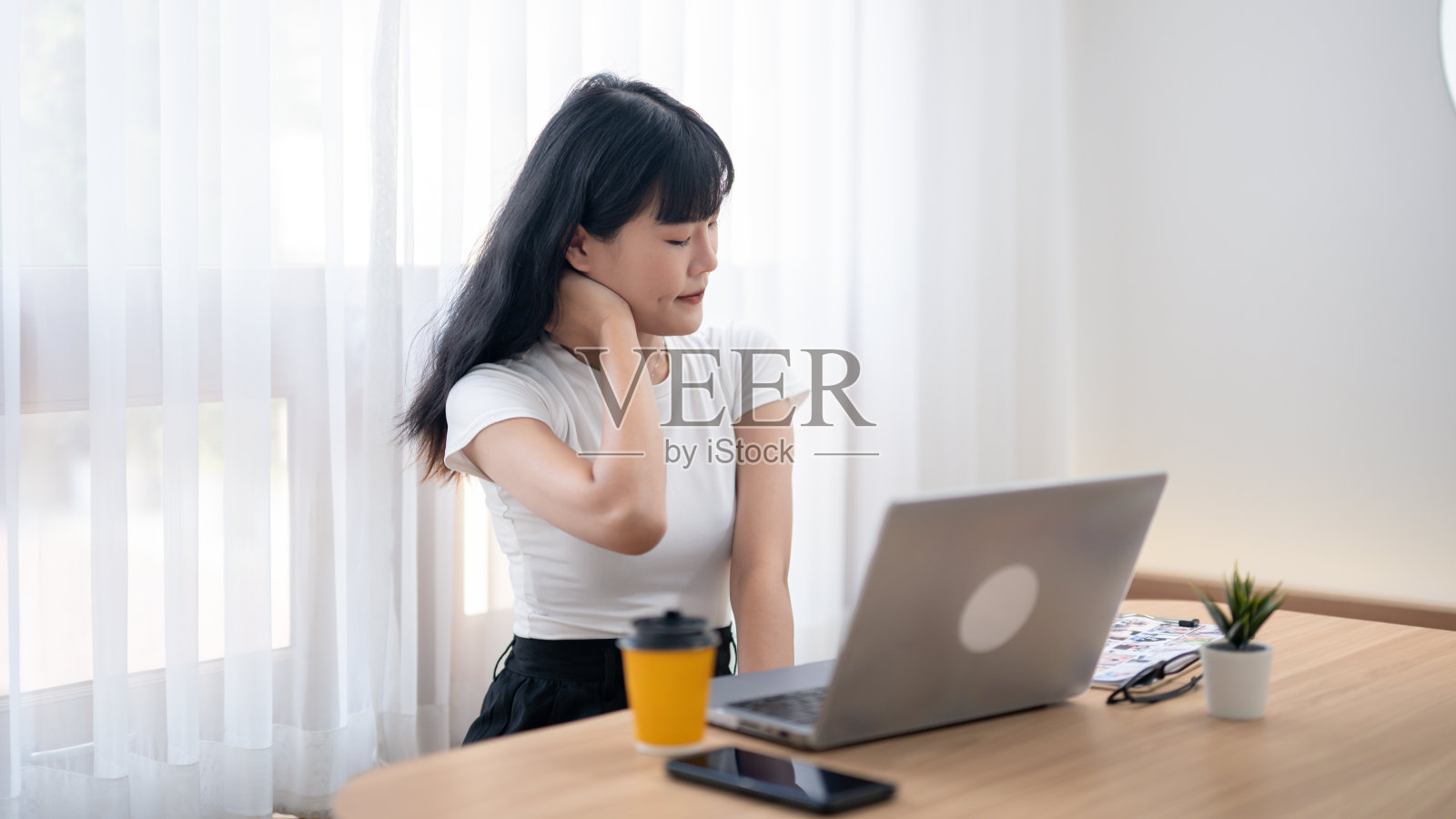 放松的亚洲女性在办公桌前休息时伸展脖子，旁边有一台笔记本电脑。照片摄影图片