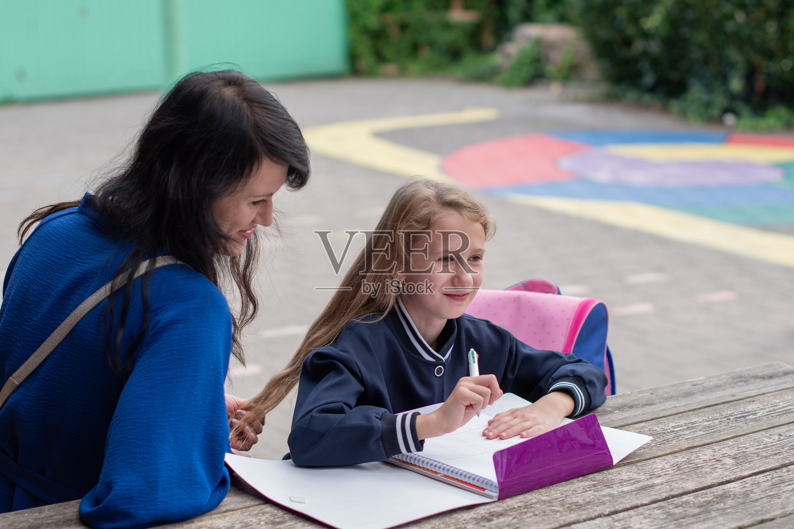 聪明的女孩独自做作业，母亲坐在旁边观看，教育概念，开学季，女孩穿着漂亮的蓝色校服，背着粉色书包照片摄影图片