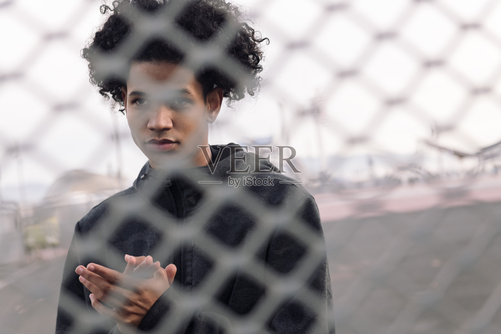 在金属链条围栏后面的卷发少年照片摄影图片