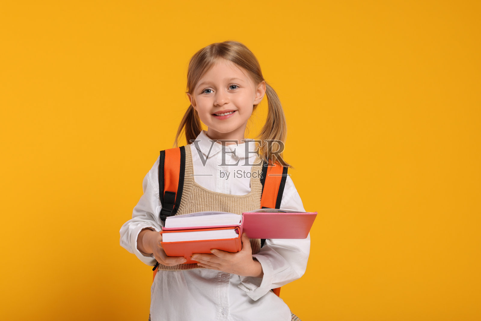 快乐的女学生背着书包和书籍，背景为橙色照片摄影图片