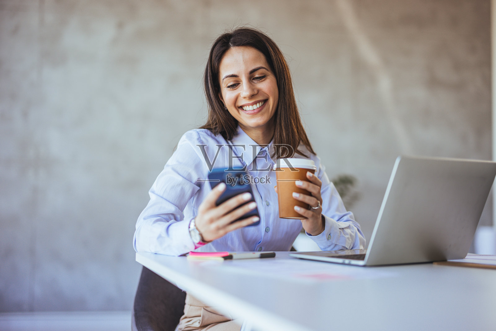 微笑的女性在办公室使用智能手机并拿着咖啡照片摄影图片
