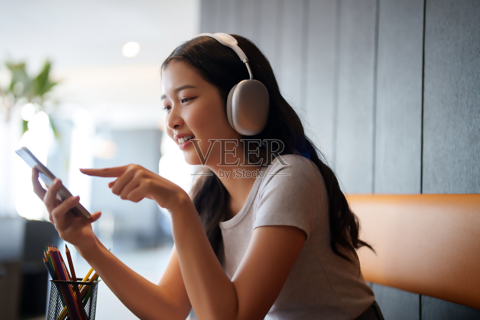 亚洲女学生戴着耳机，听音乐并在咖啡馆用智能手机与朋友聊天，放松心情，备考学习知识。照片摄影图片