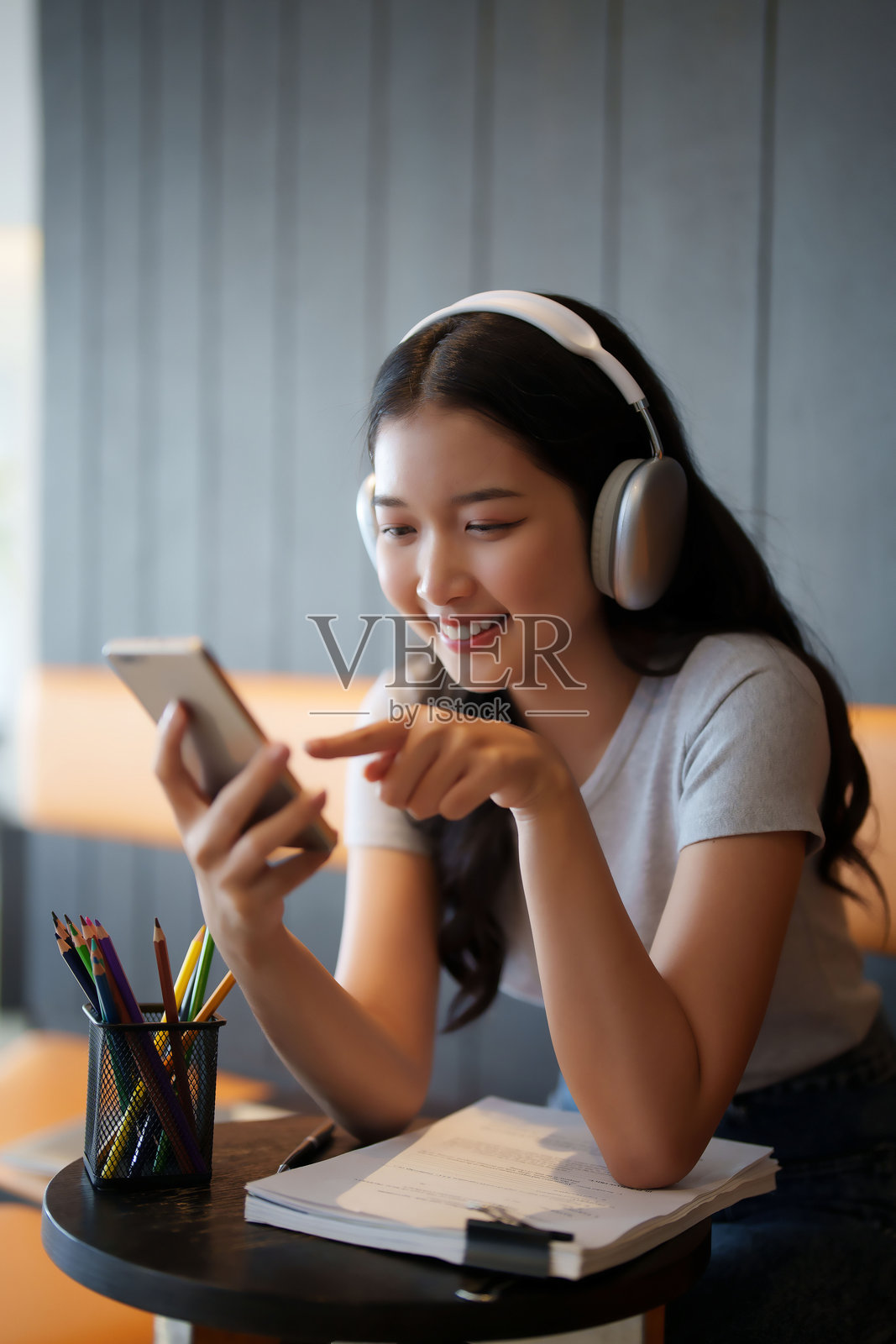 亚洲女学生戴着耳机，听音乐并在咖啡馆用智能手机与朋友聊天，放松心情，备考学习知识。照片摄影图片