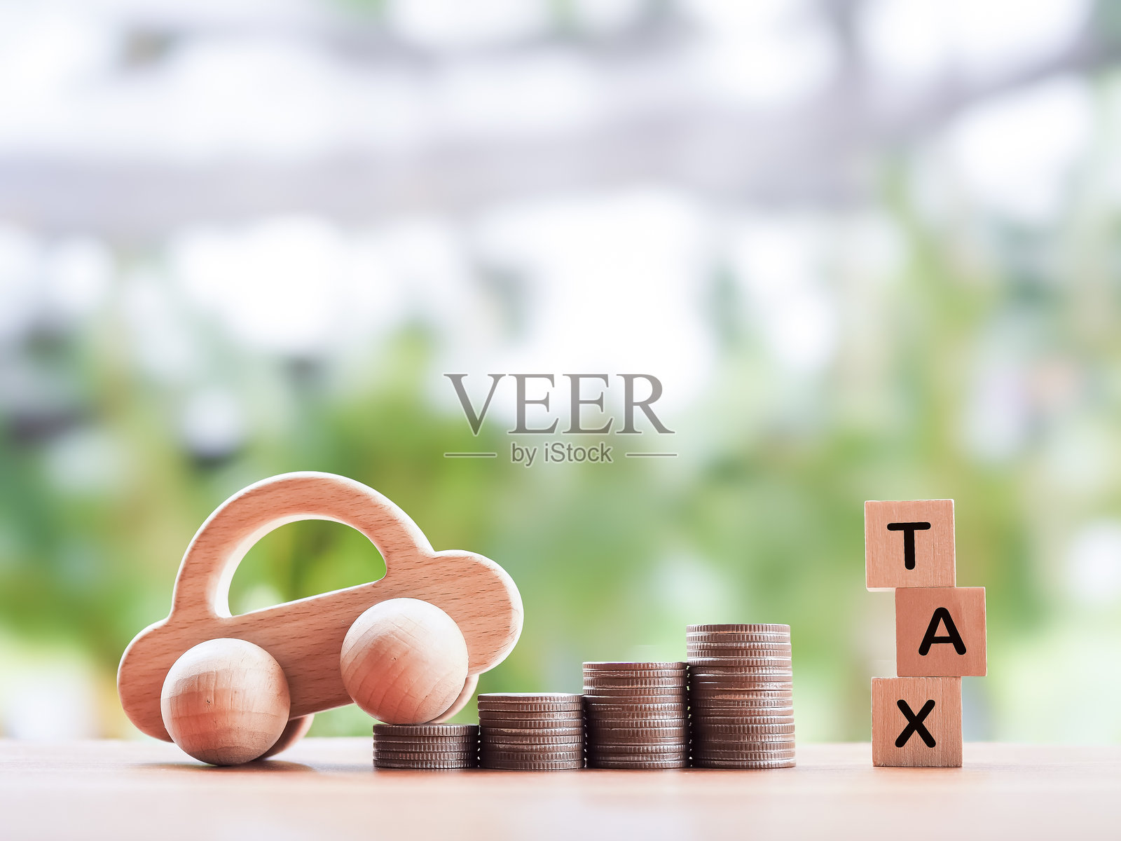 木制玩具车，带有“TAX”字样的木块和一堆硬币。节省和管理资金以实现成功交通的概念，支付税款和汽车贷款。照片摄影图片
