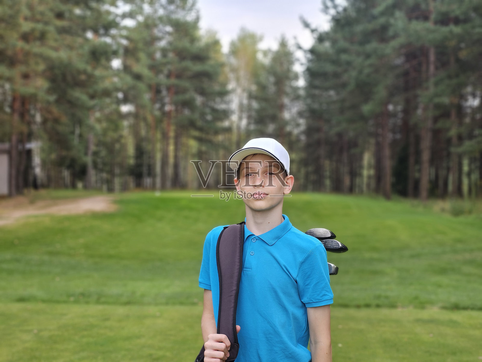 年轻高尔夫球手准备在绿草如茵的球场上打球，背景是高大的树木。照片摄影图片