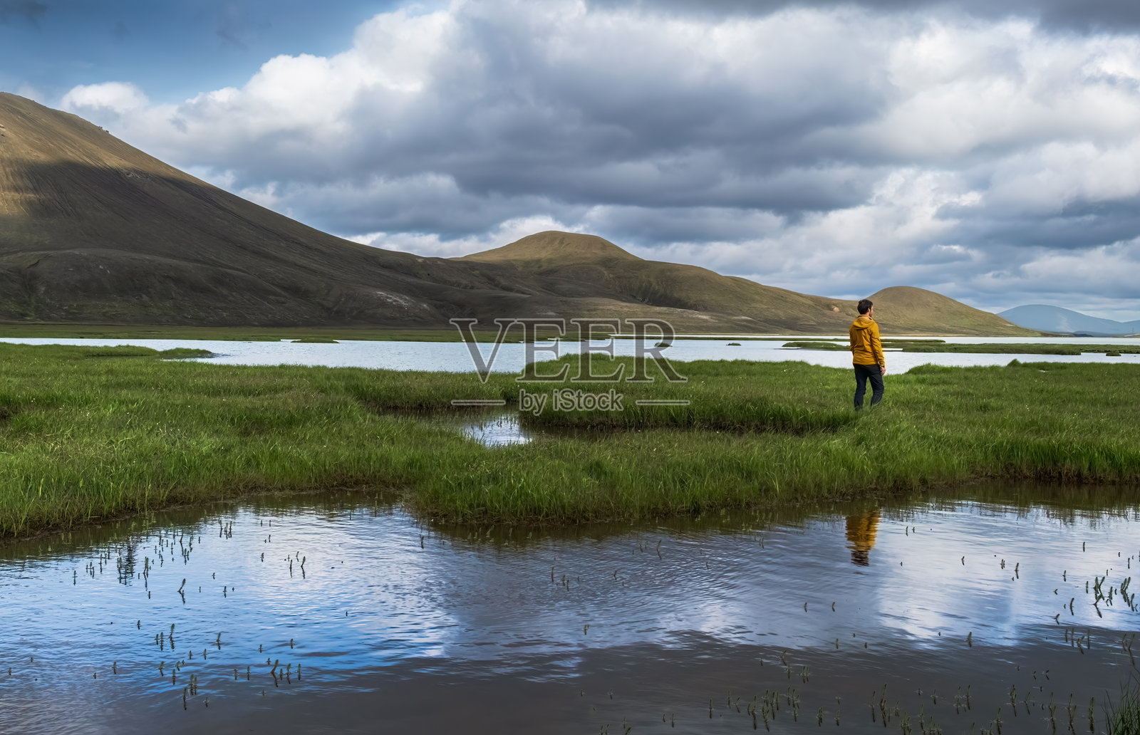 冰岛高地的山脉和沼泽景观，远处有一位男子在凝视远方。照片摄影图片
