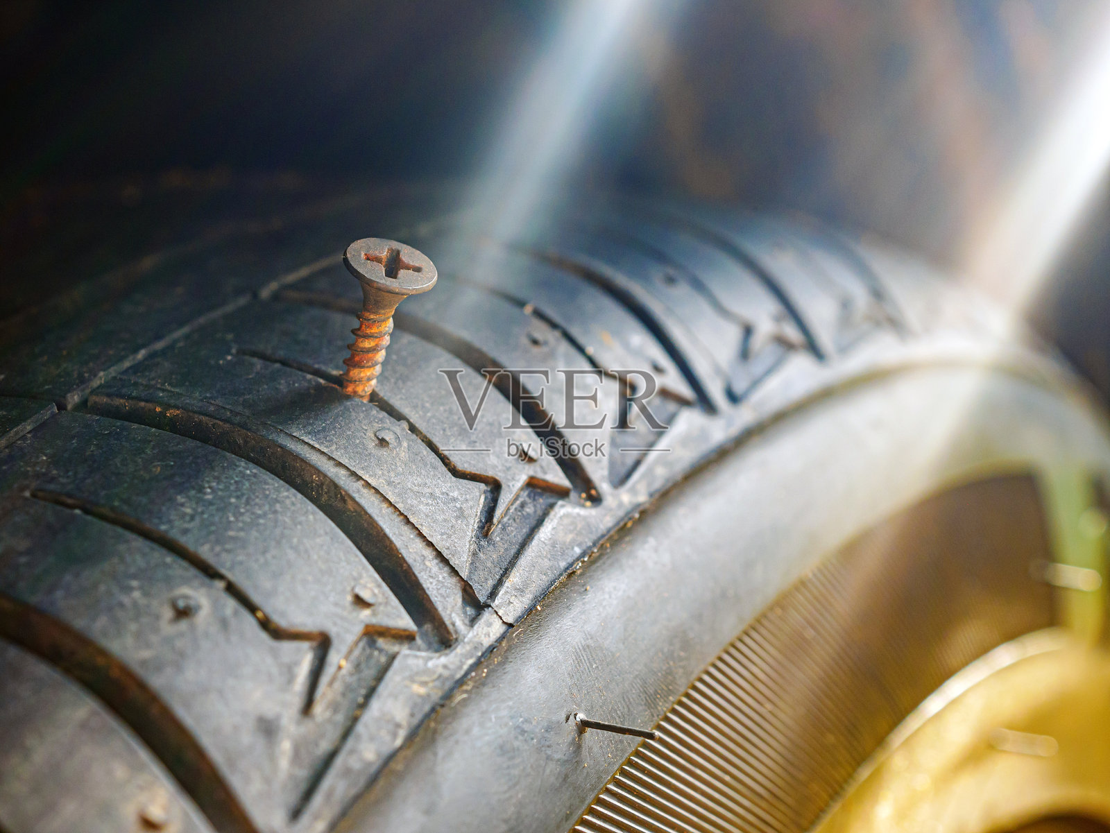 生锈的螺丝钉特写，正在刺入汽车轮胎造成穿刺。照片摄影图片