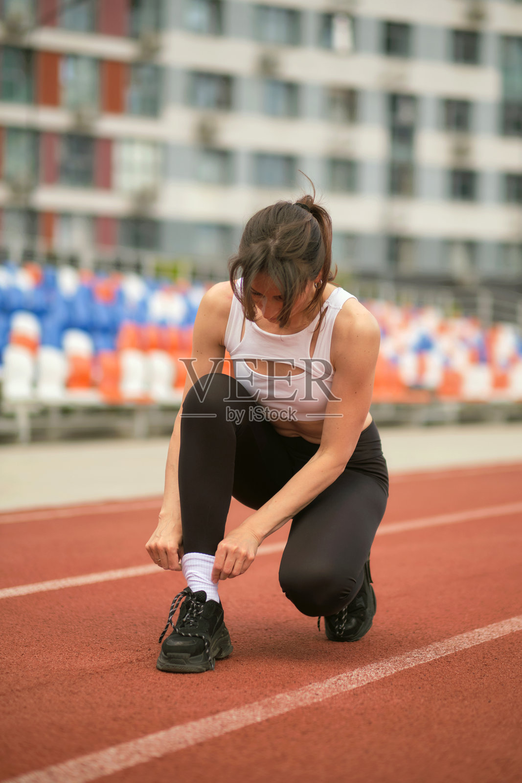 这位运动女性在跑道上系鞋带，为锻炼做好准备，她坚定的表情彰显了她的专注与奉献。这张图片捕捉了健身中准备和专注的本质。照片摄影图片